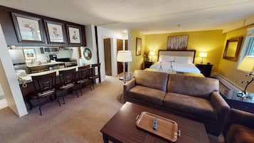 A hotel room with a kitchenette, a sofa, a dining area, and a bed.