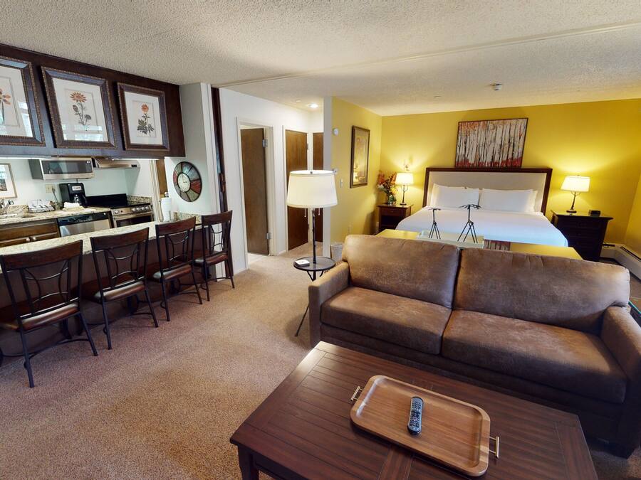 A hotel room with a kitchenette, a sofa, a dining area, and a bed.