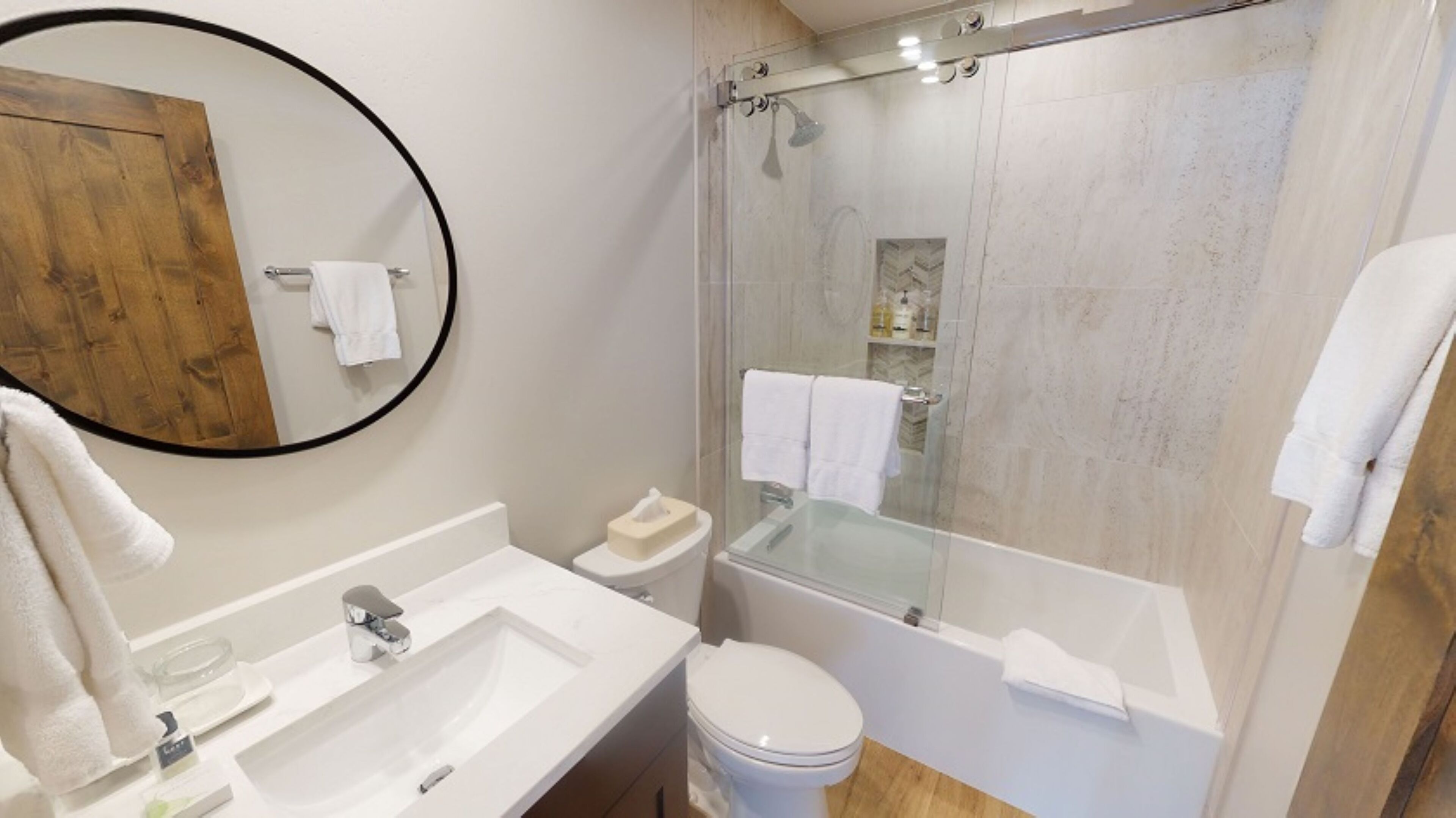A modern bathroom with a glass-enclosed shower, a round mirror, a white sink, and a toilet.