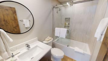 A modern bathroom with a glass-enclosed shower, a round mirror, a white sink, and a toilet.