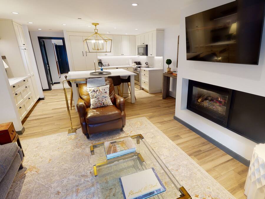A modern living room with a fireplace, leather sofa, and a dining area with a white table and chairs.