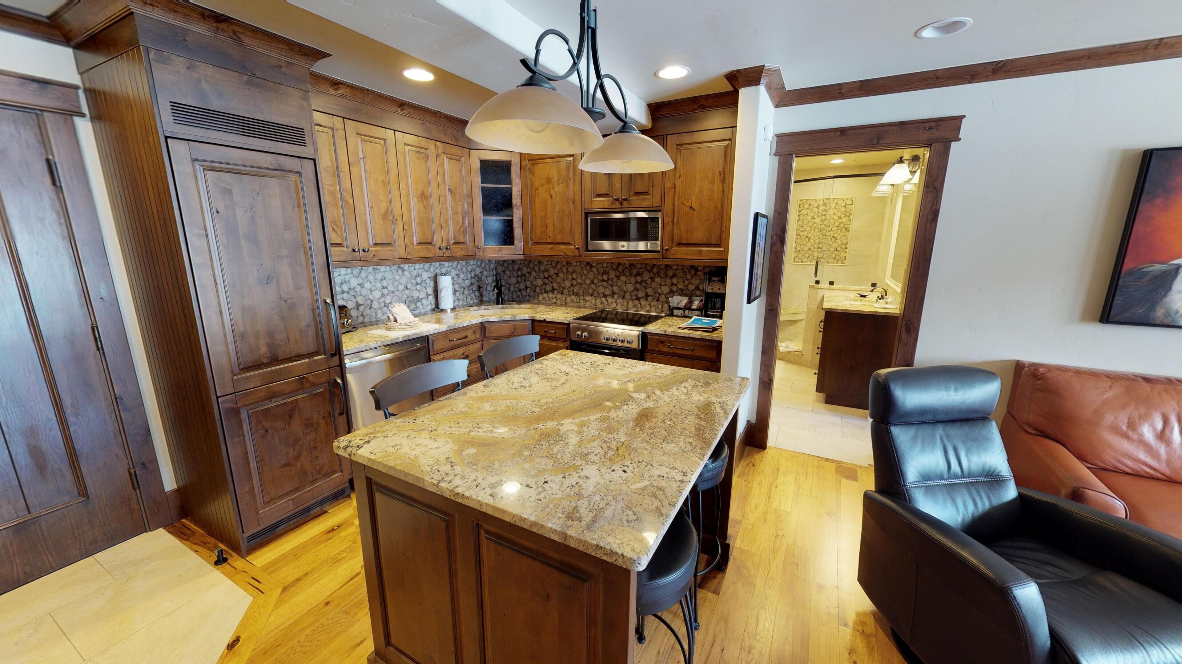 A kitchen with wooden cabinets, granite countertops, a central island, and a dining area with a leather chair.