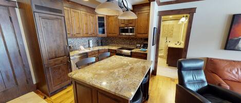 A kitchen with wooden cabinets, granite countertops, a central island, and a dining area with a leather chair.