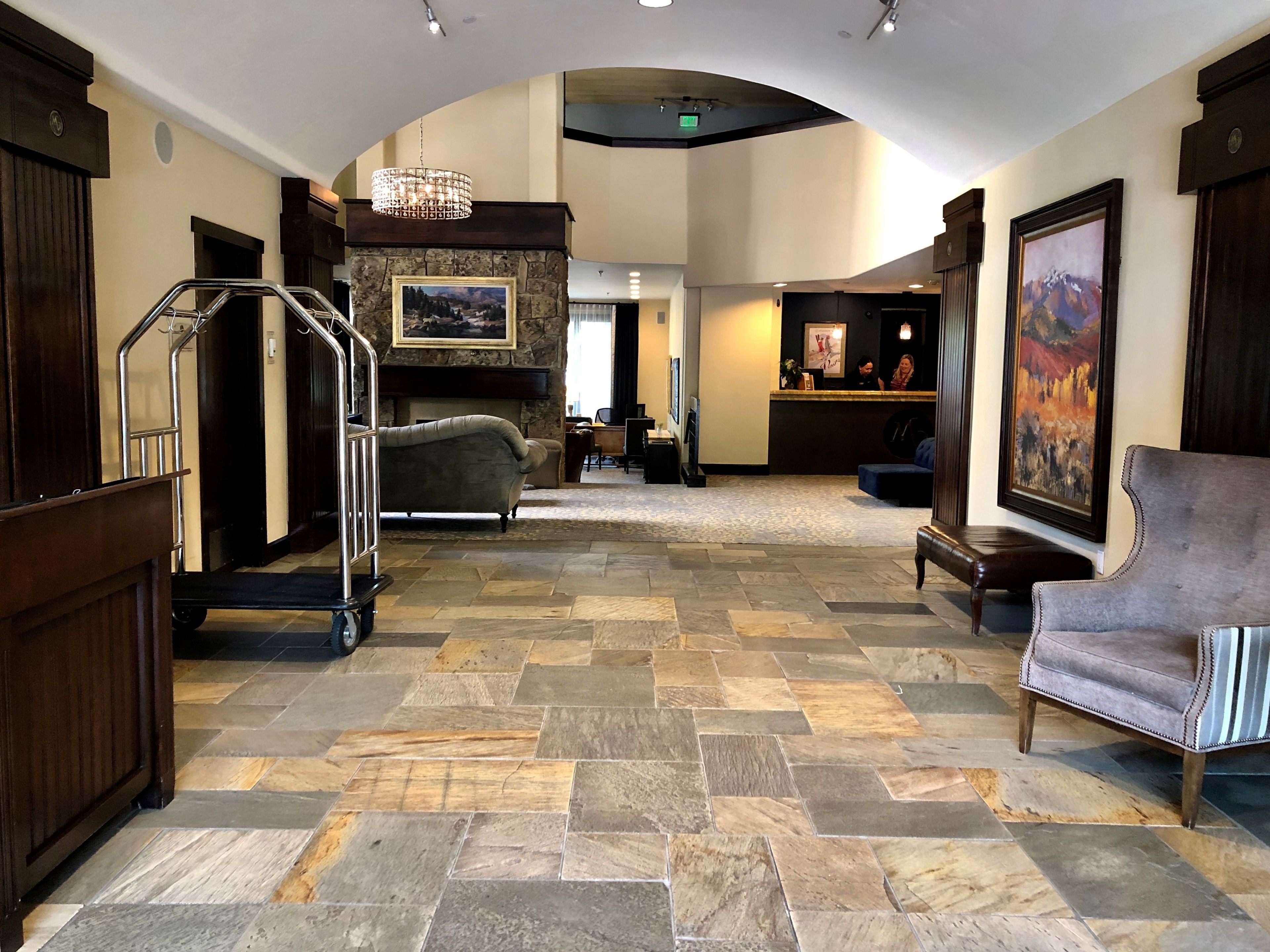 A lobby with a stone-tiled floor, a reception desk, a fireplace, and a large painting.