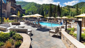 A poolside area with lounge chairs and umbrellas, surrounded by stone walls and greenery, with a mountain backdrop.