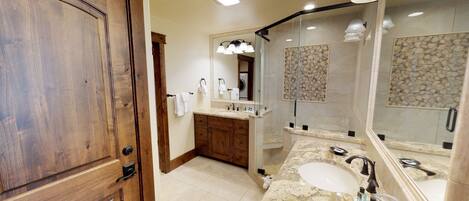 Un baño moderno con puerta de madera, tocador con lavabo y espejo, y zona de ducha con pared de piedra.