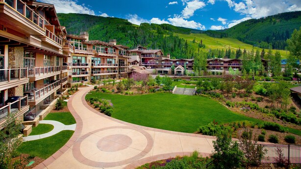 A resort with multiple buildings, a central lawn, and a mountainous backdrop.