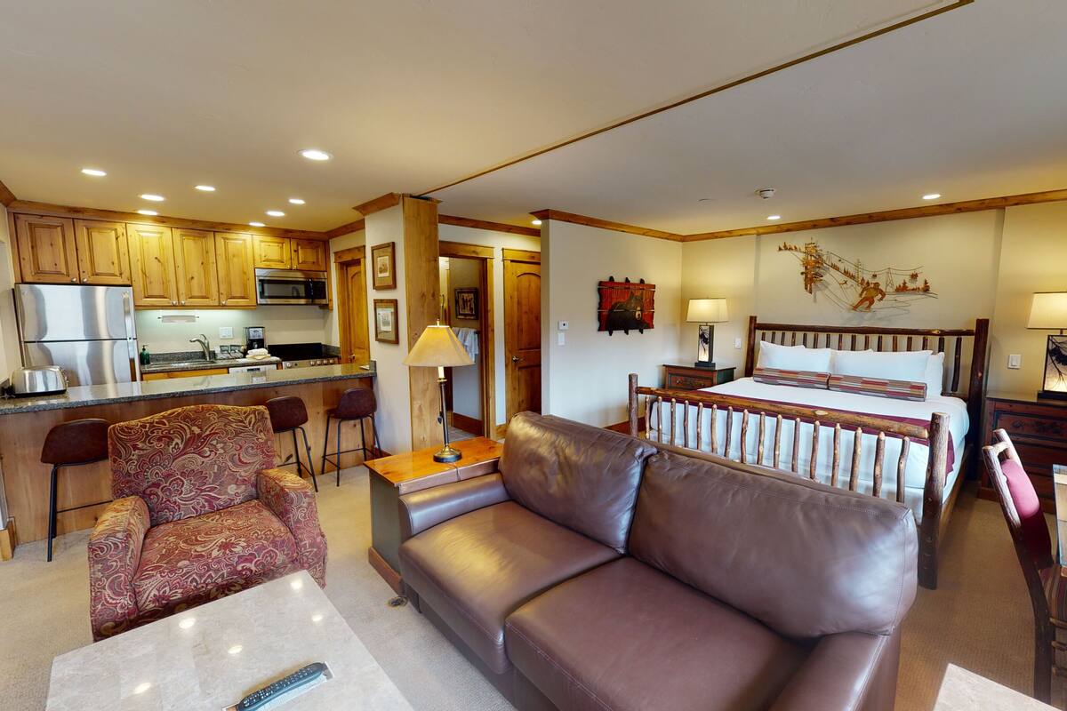 Una habitación de hotel moderna con kitchenette, un sofá, una cama y una zona de comedor.