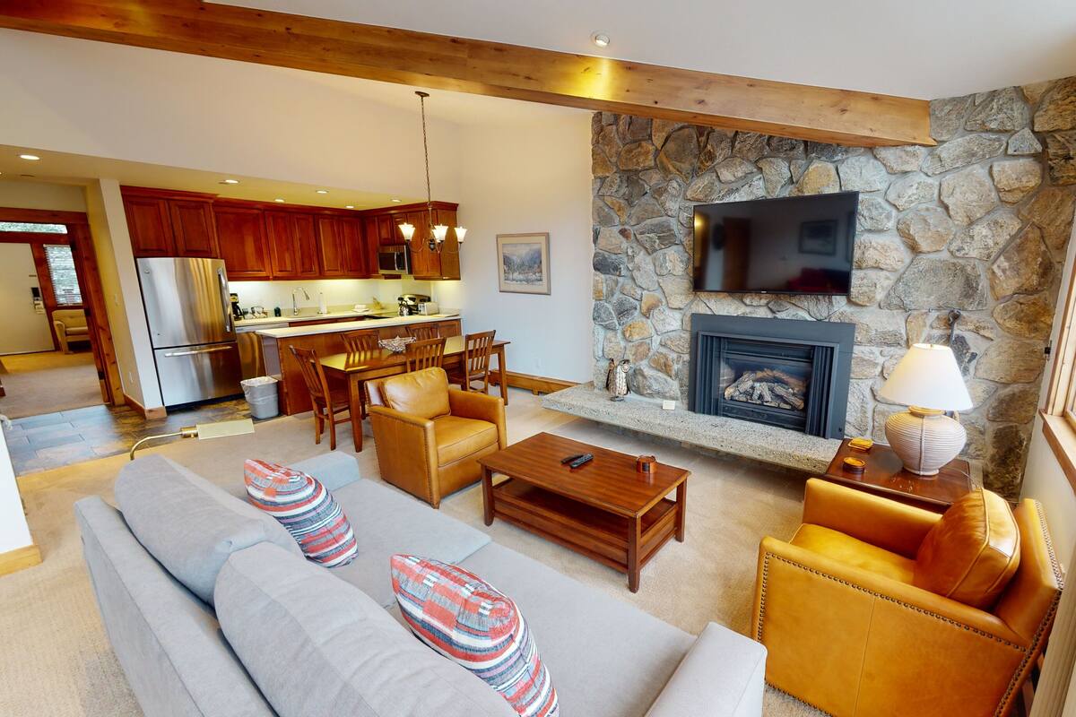 Una sala de estar moderna con chimenea de piedra, un televisor de pantalla plana montado encima y un rincón de descanso acogedor con sofá y sillones.