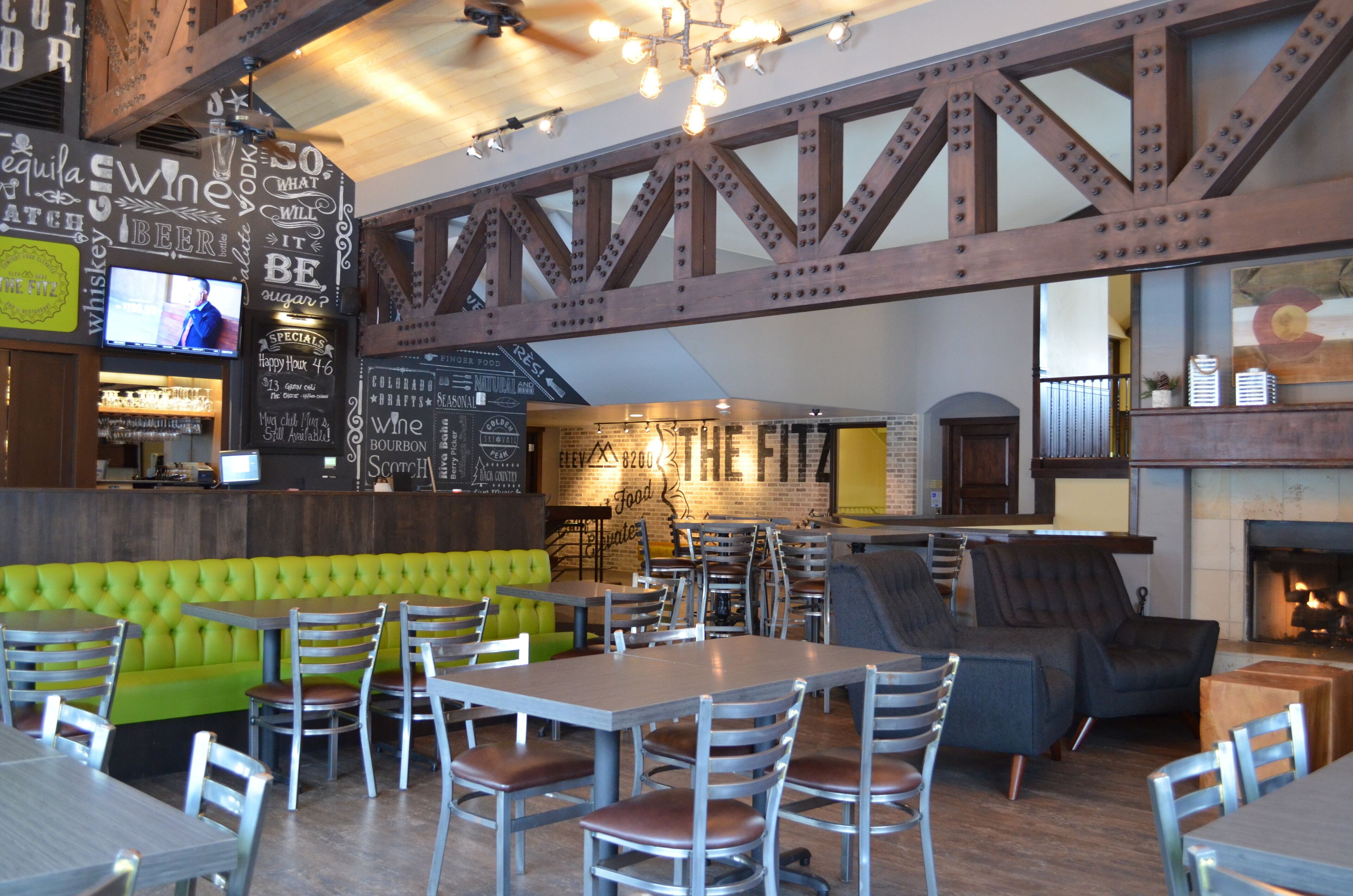 A restaurant with a green booth seating area, multiple tables, and a brick wall with menu options.