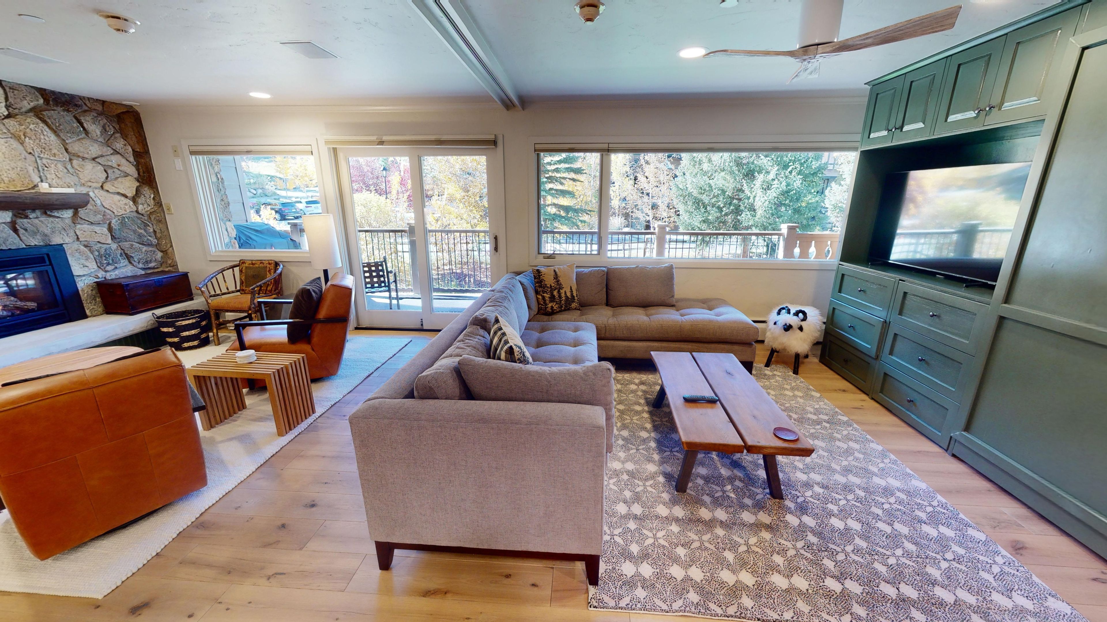A modern living room with a stone fireplace, large windows, a flat-screen TV, and a cozy seating area.