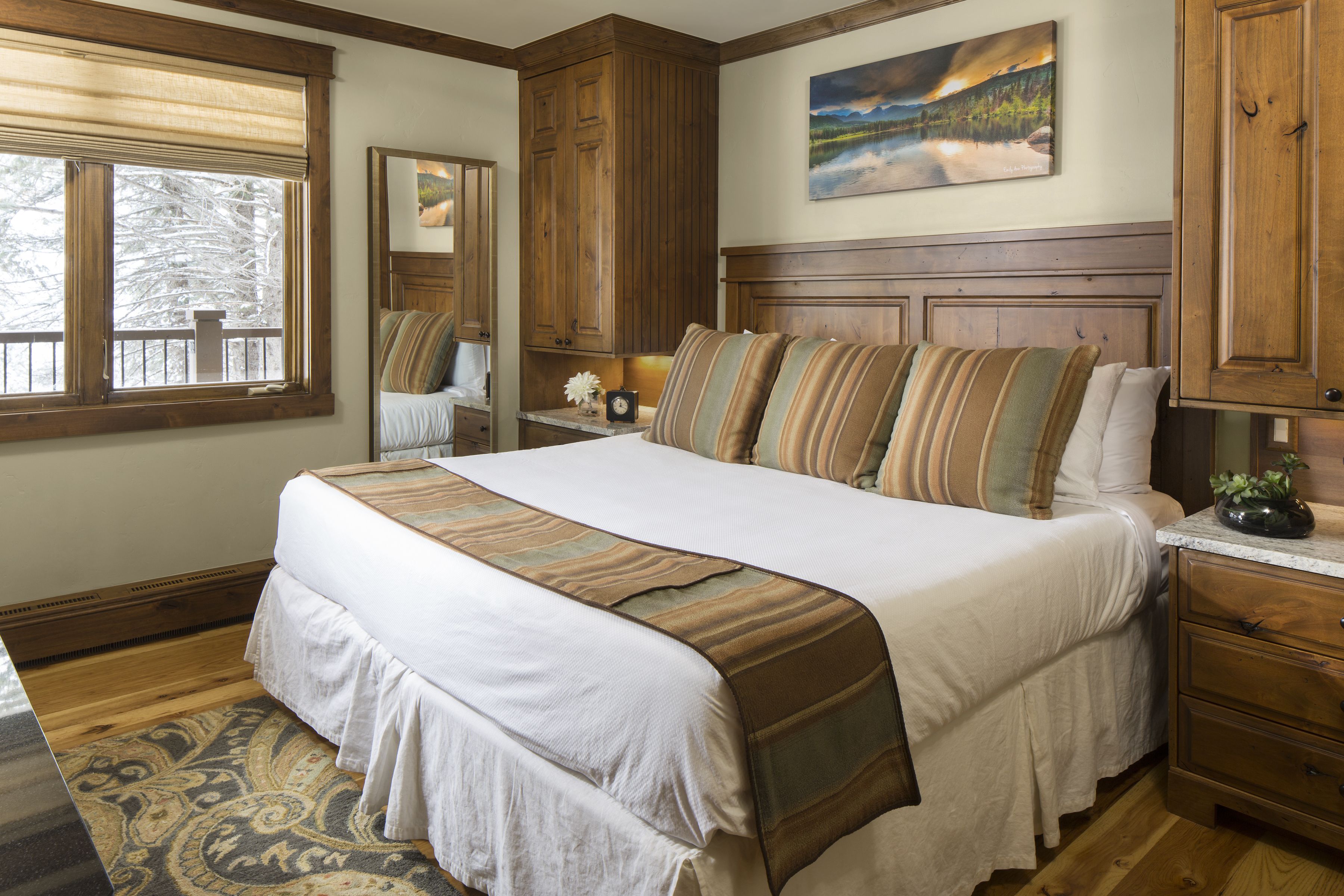 Uma cama grande com colcha listrada, cabeceira de madeira e mesa de cabeceira com abajur.