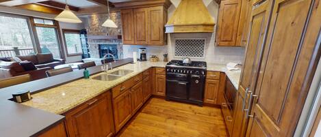 A kitchen with wooden cabinets, a granite countertop, a stove, and a large window overlooking a patio area.