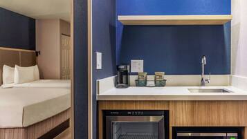 A hotel room with a bed, a kitchenette with a coffee maker, a microwave, and a refrigerator.