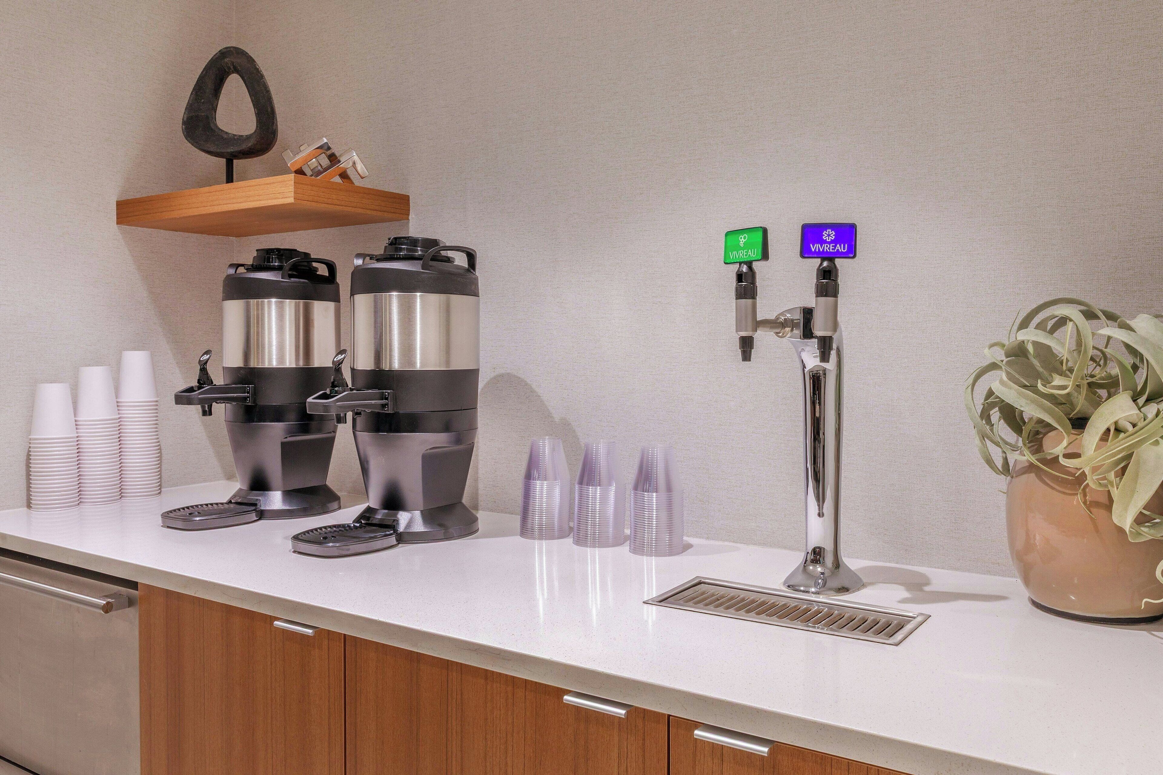 A coffee station with two coffee dispensers, a water dispenser, and a potted plant.