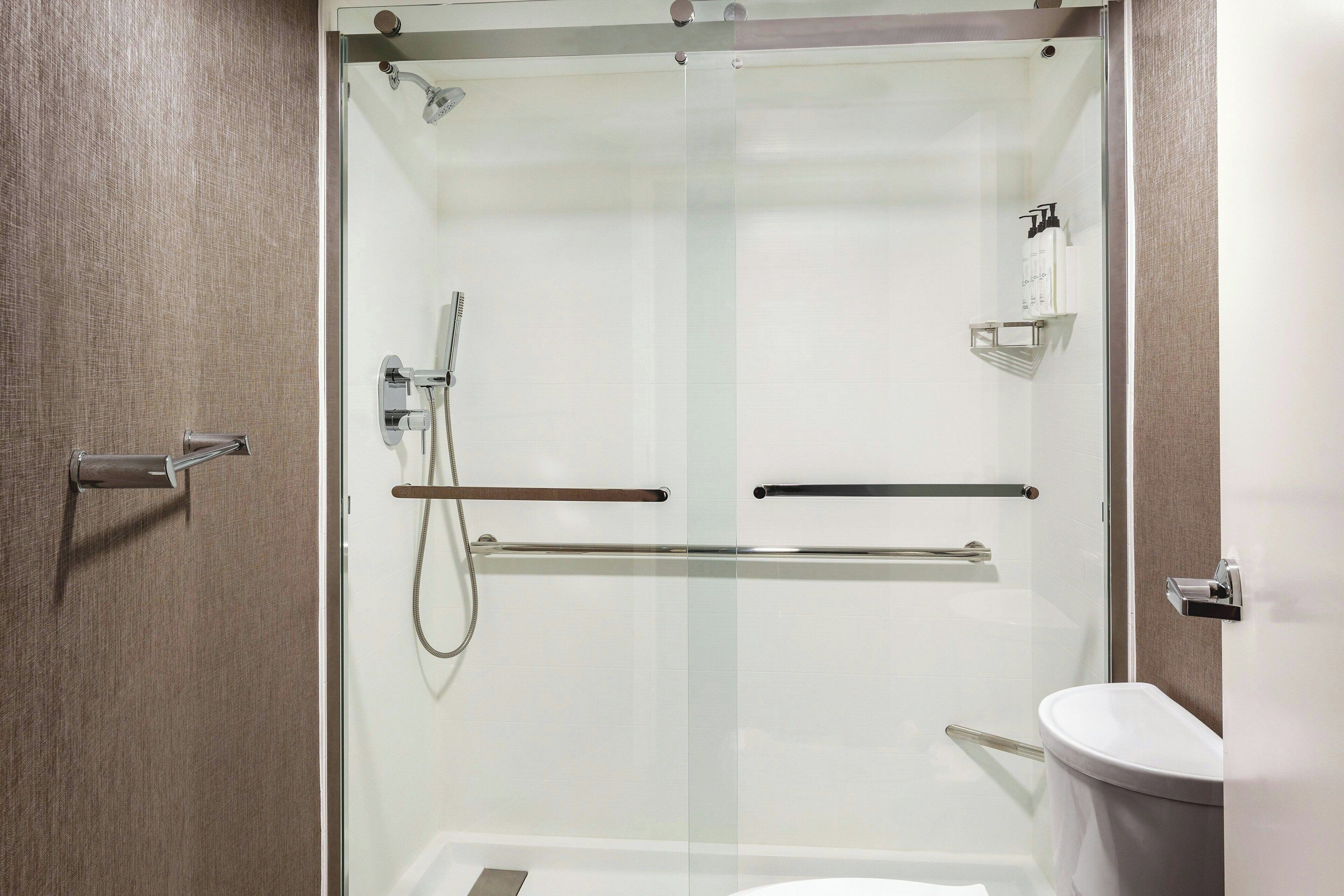 A modern bathroom with a glass-enclosed shower, a toilet, and a shelf with toiletries.