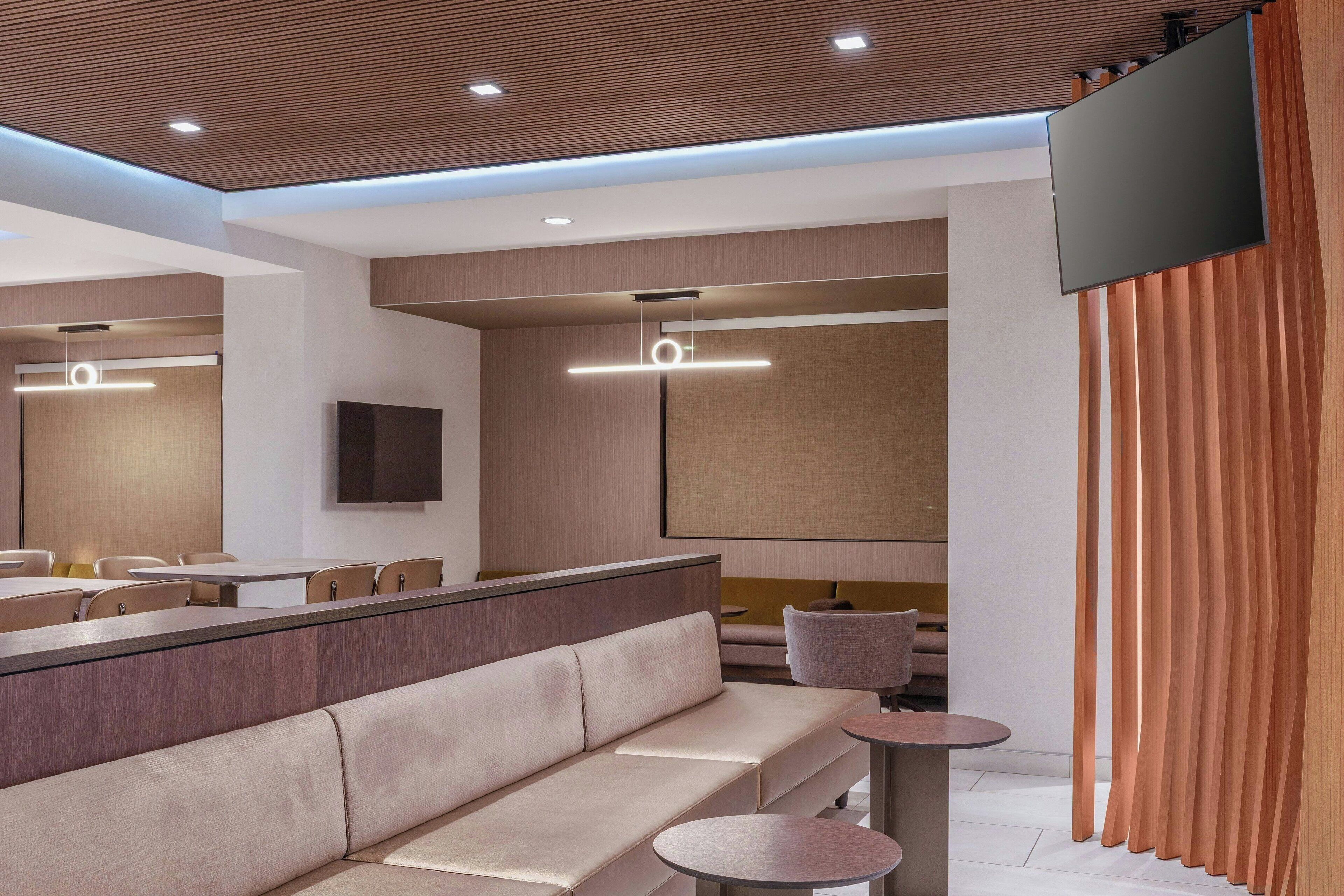 A modern hotel lobby with a sofa, tables, and a TV.