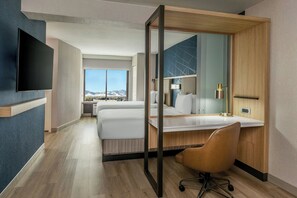 Ein modernes Hotelzimmer mit einem großen Bett, einem Schreibtisch mit Stuhl, einem Flachbildfernseher und einem großen Fenster mit Blick auf die Berge.