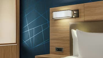 A hotel room with a bed, a nightstand, a wall-mounted light, and a power outlet.