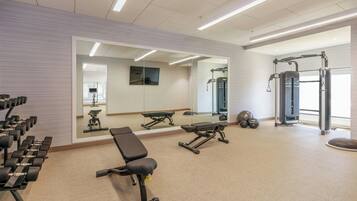 Ein Fitnessraum mit Trainingsgeräten, einer Bank und einem Spiegel.