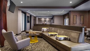 Um hall de hotel moderno com um sofá modular, uma mesa redonda e uma TV de tela plana fixada na parede.