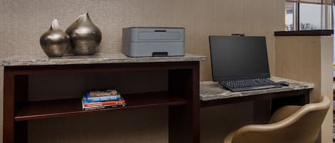 Un espacio de trabajo en un hotel con computadora de escritorio, impresora y objetos decorativos sobre un mostrador.