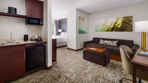 Quarto de hotel compacto com cozinha compacta, sofá, escrivaninha e uma grande pintura abstrata na parede.