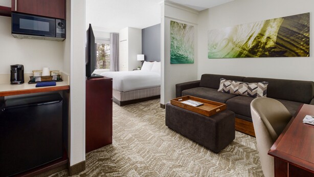 Quarto de hotel com cozinha compacta, cama, sofá, mesa de centro e uma grande pintura abstrata.