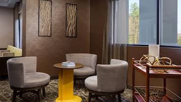 A hotel room with two grey armchairs, a small yellow table, and a decorative metal piece on a wooden table.