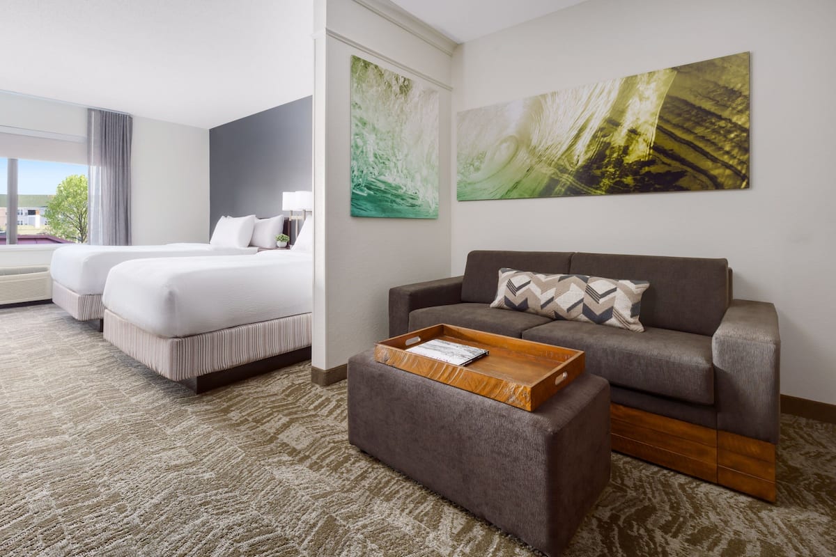 A hotel room with two beds, a sofa, a wooden tray table, and abstract wall art.