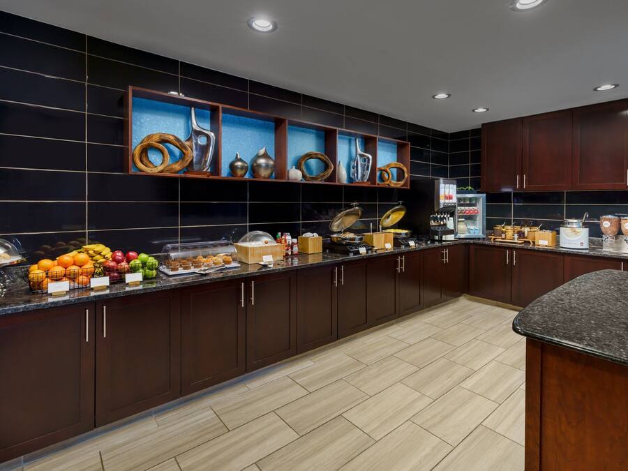 A modern kitchen with dark wooden cabinets, a marble countertop, and various food items displayed.