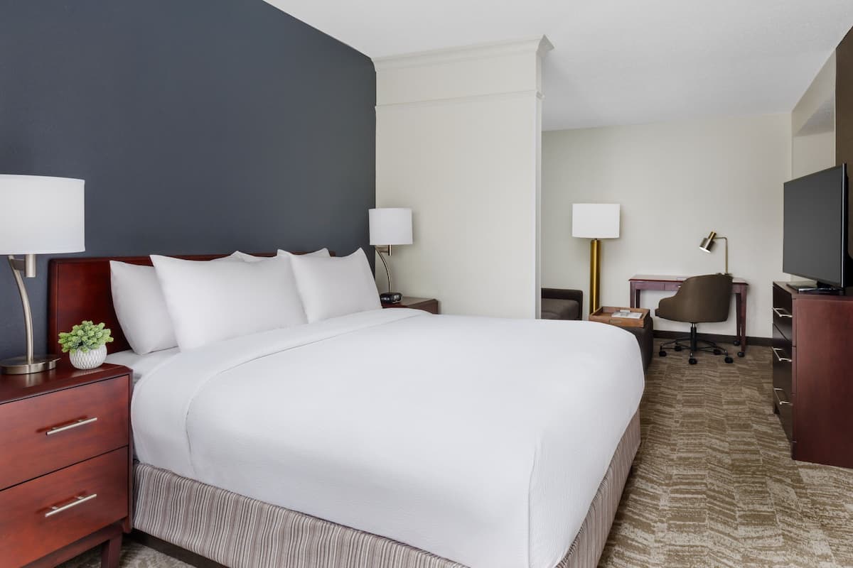 A hotel room with a large bed, bedside tables, a desk, a chair, and a television.