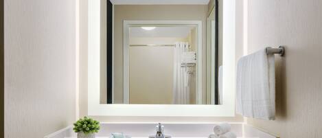 A modern bathroom with a large mirror, a sink, a small potted plant, and neatly folded towels.