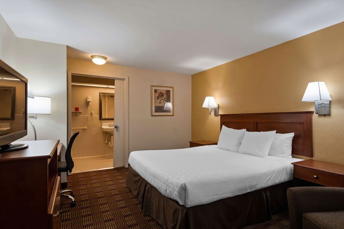 A hotel room with a bed, desk, chair, and a bathroom visible through an open door.