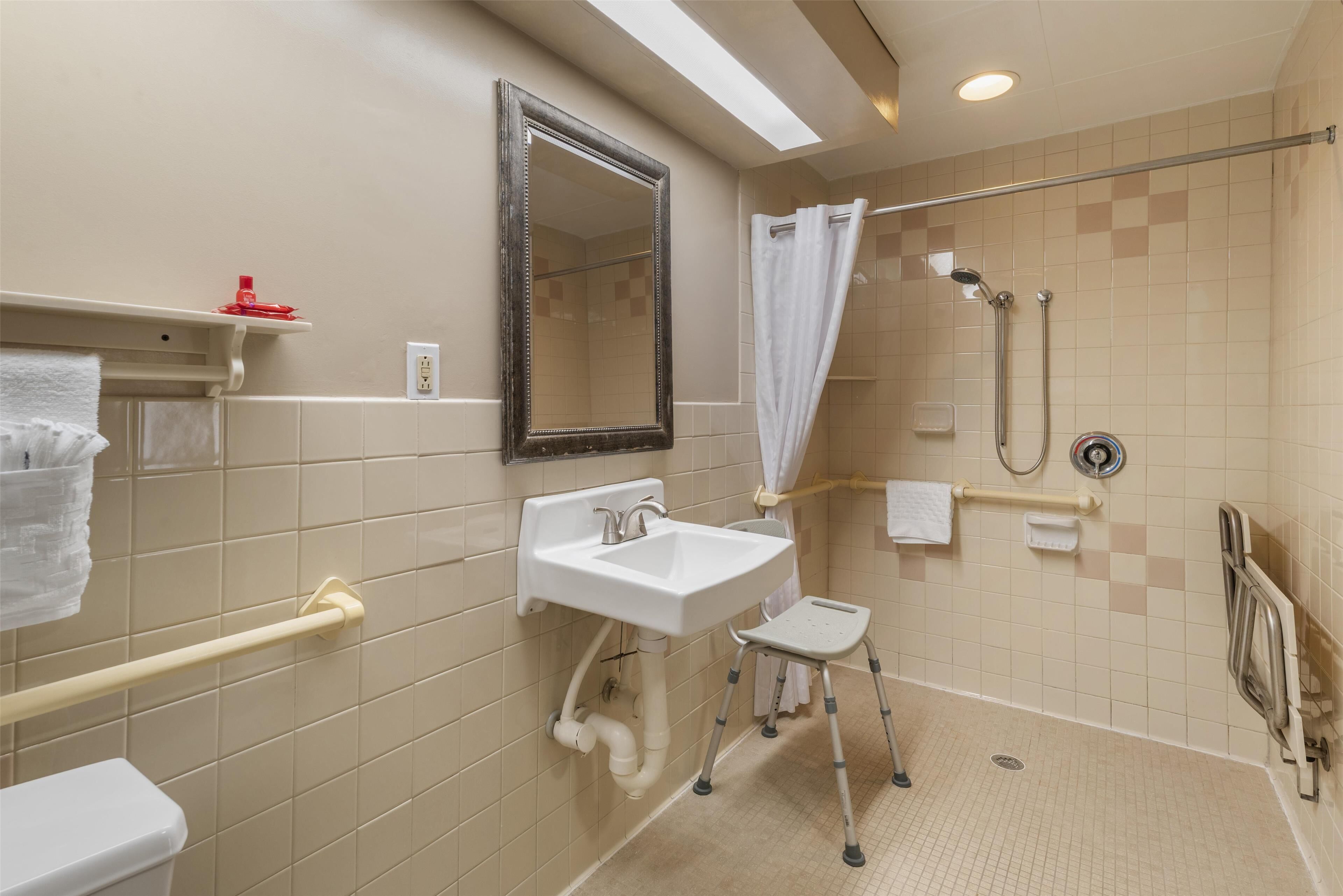 A bathroom with a white sink, a mirror, a shower with a curtain, and a grab bar.