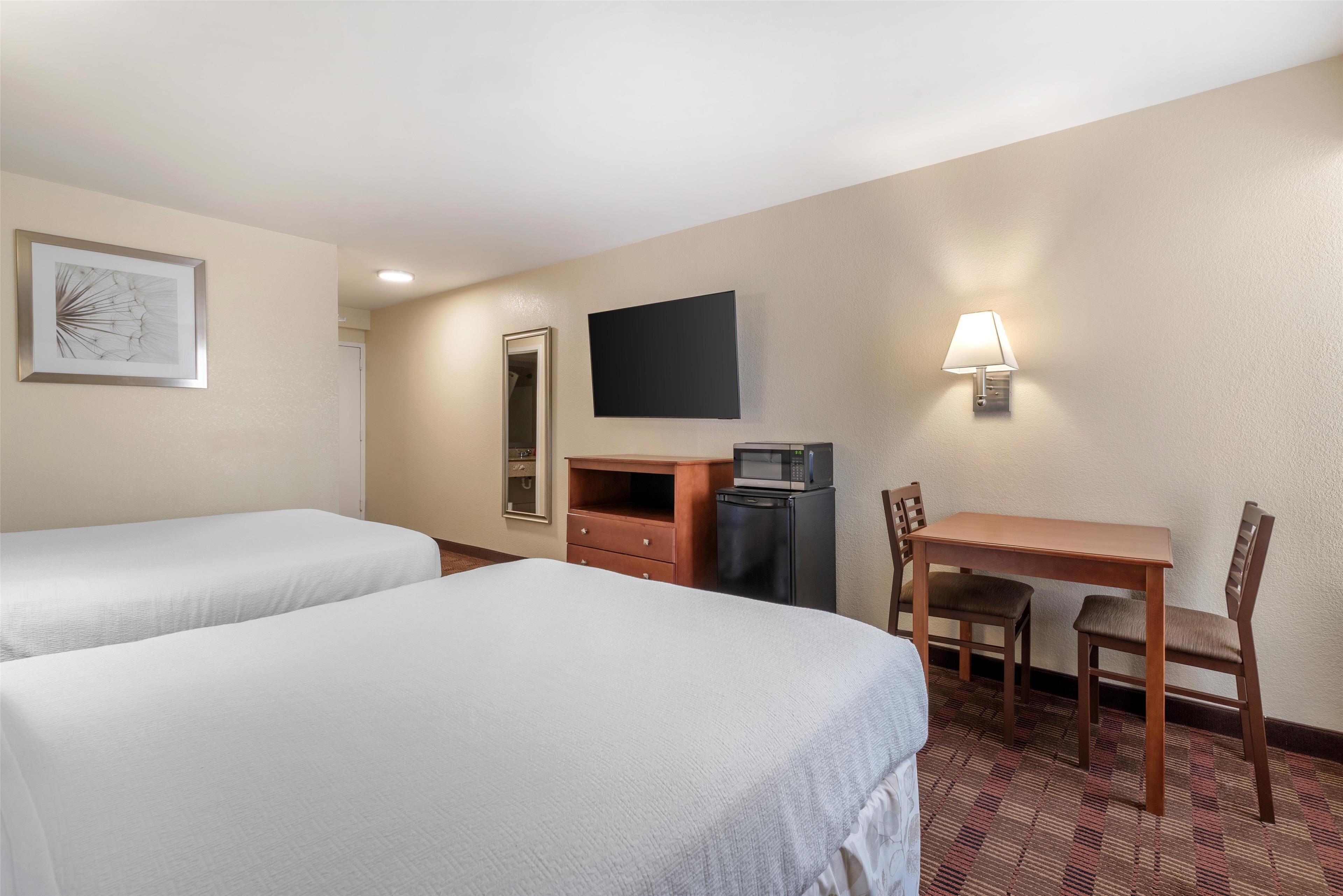 A hotel room with two beds, a desk, a chair, a TV, a microwave, and a dresser.