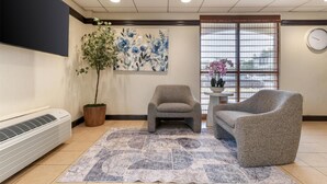 A room with a large air conditioner, a potted plant, two armchairs, a patterned rug, and a wall-mounted clock.