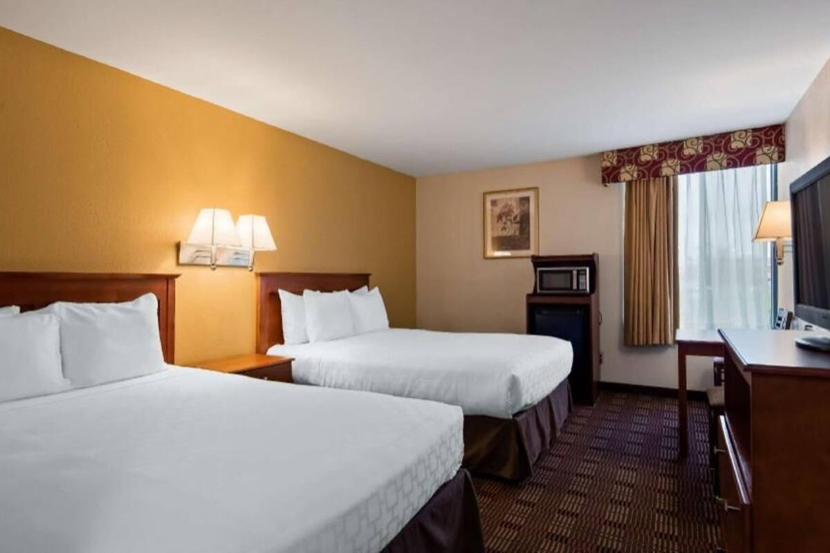 Ein Hotelzimmer mit zwei Betten, einem Fernseher, einer Mikrowelle und einem Schreibtisch.