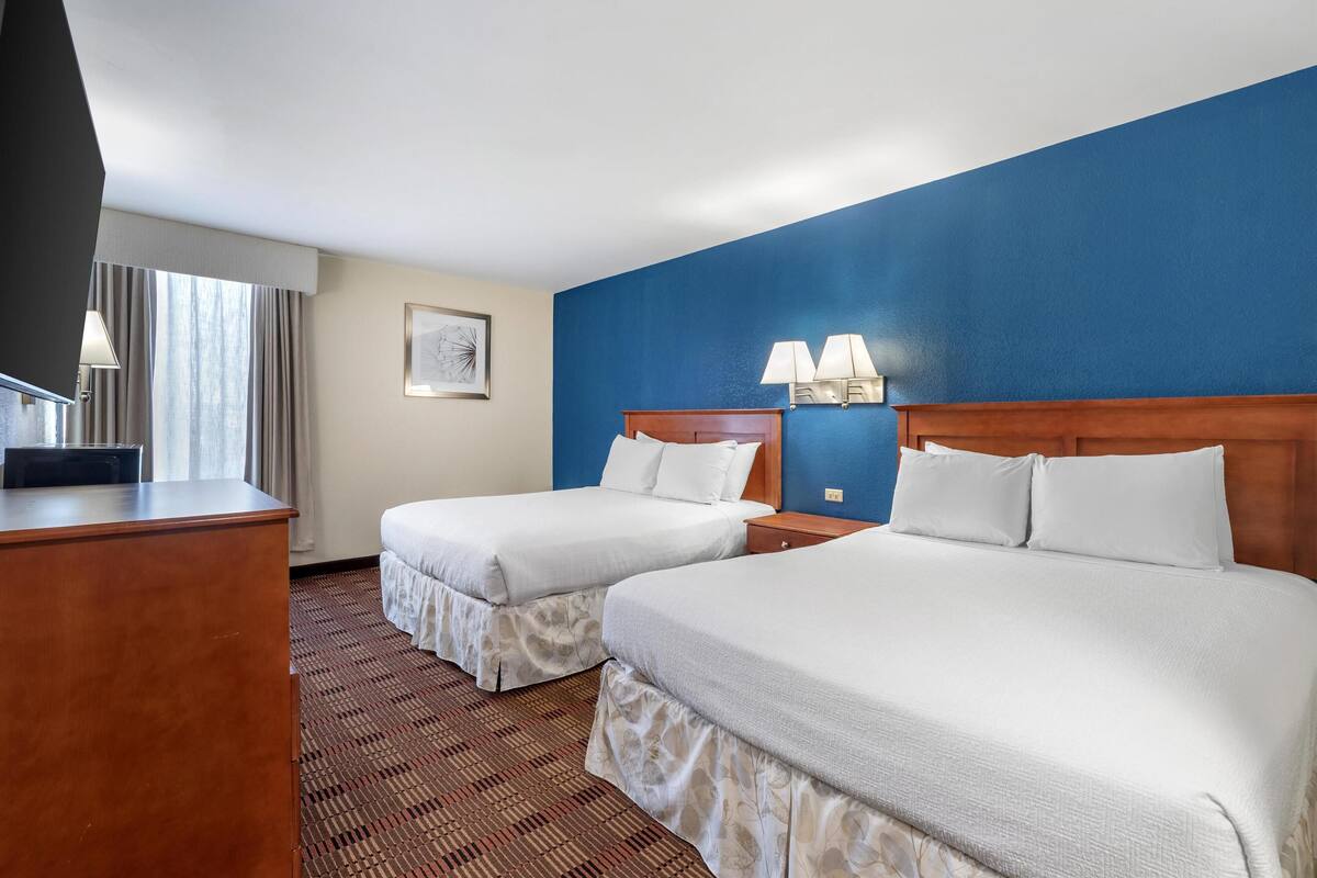 Ein Hotelzimmer mit zwei Betten, einem Schreibtisch, einem Fernseher und einem Fenster mit Vorhängen.