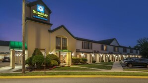 A SureStay hotel by Best Western with a green awning, an office entrance, and a parking lot with cars.