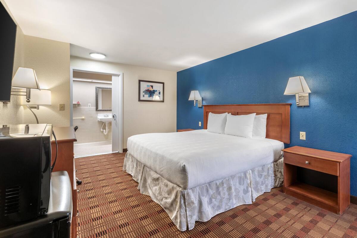 Una habitación de hotel con una cama grande, dos mesitas de noche, un escritorio con silla y un televisor.