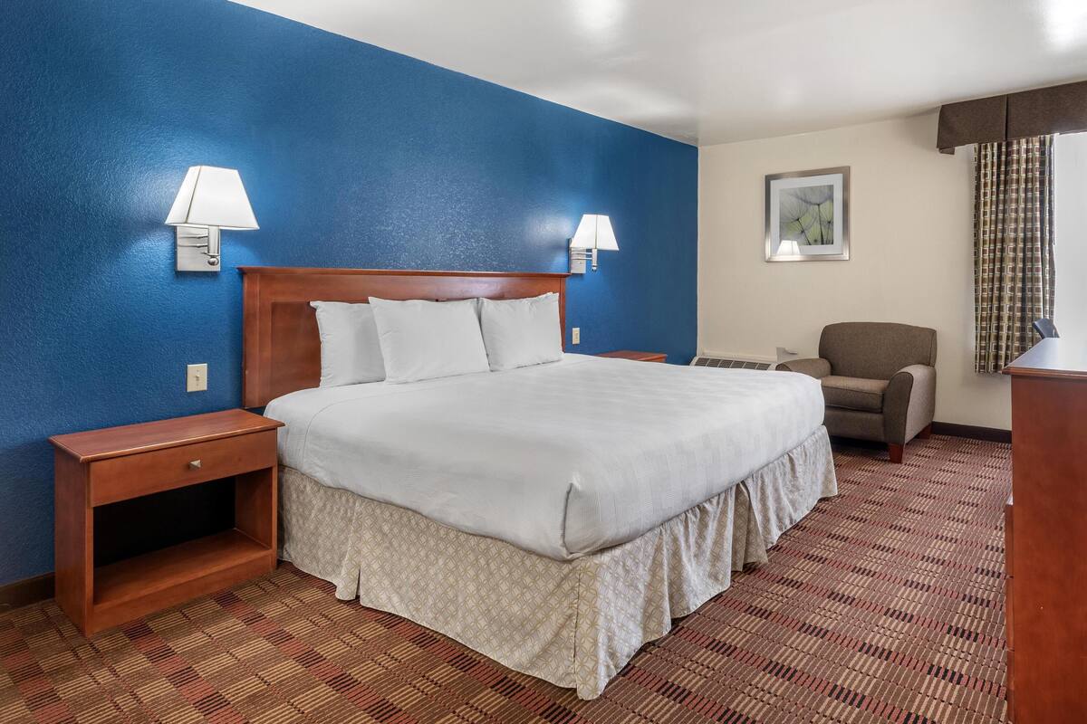 Ein Hotelzimmer mit einem großen Bett, zwei Nachttischlampen, einem Sessel und einem Schreibtisch.