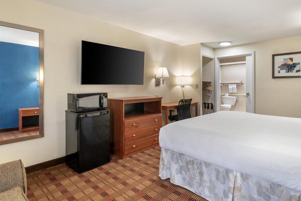 Une chambre d’hôtel équipée d’un lit, d’un bureau, d’une télévision, d’un réfrigérateur, d’une lampe et d’un miroir.