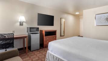 A hotel room with a bed, a desk with a computer, a microwave, a dresser, a TV, and a mirror.