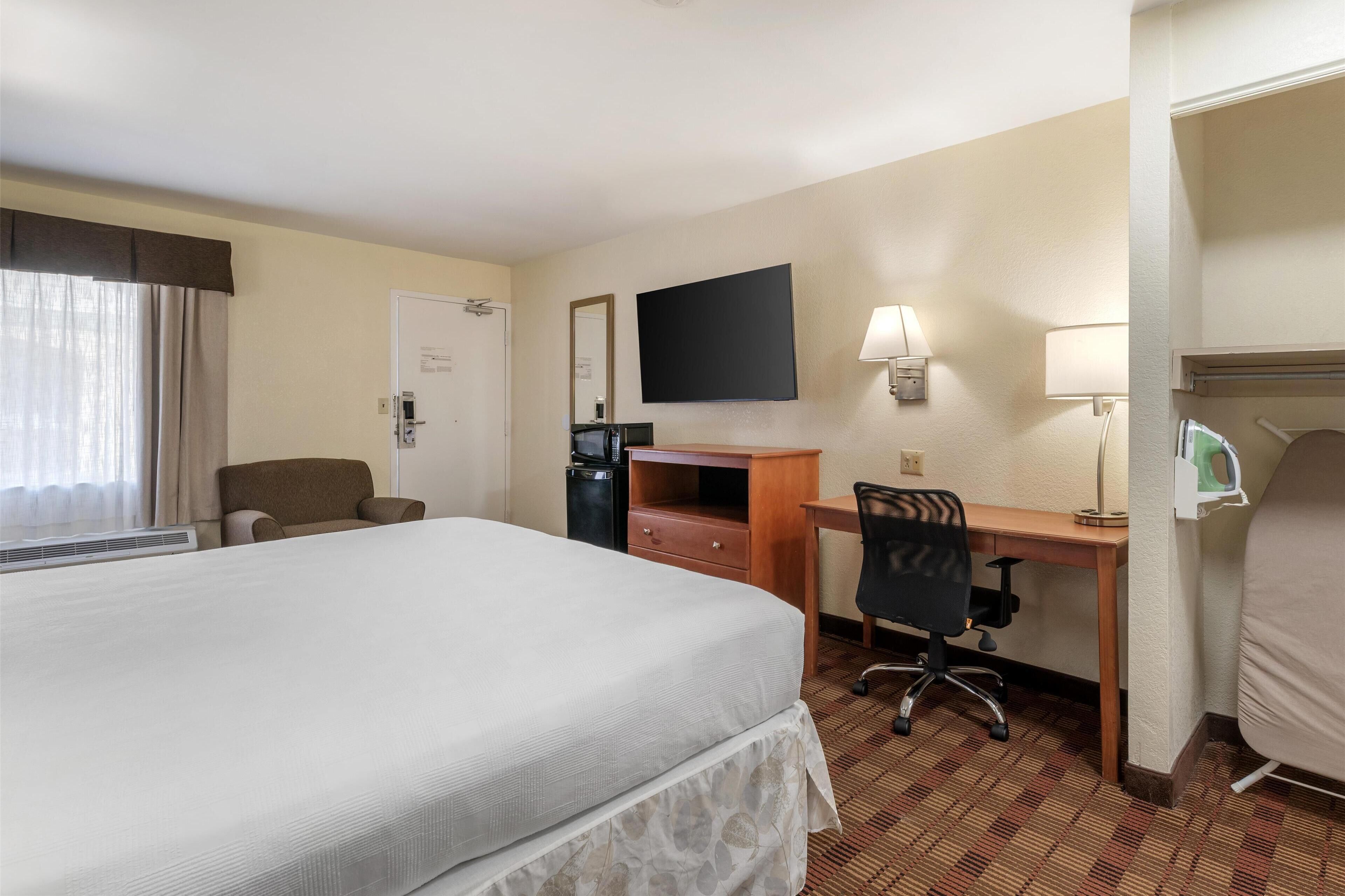 A hotel room with a bed, a desk, a chair, a TV, and a coffee machine.