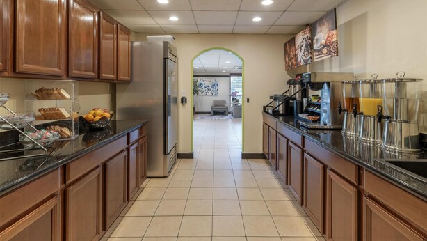 A modern kitchen with wooden cabinets, a refrigerator, a coffee station, and a fruit bowl.