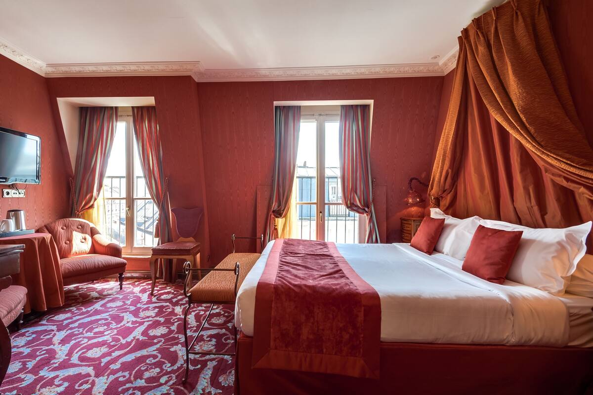A hotel room with a large bed, a desk with a chair, a television, and two windows with curtains.