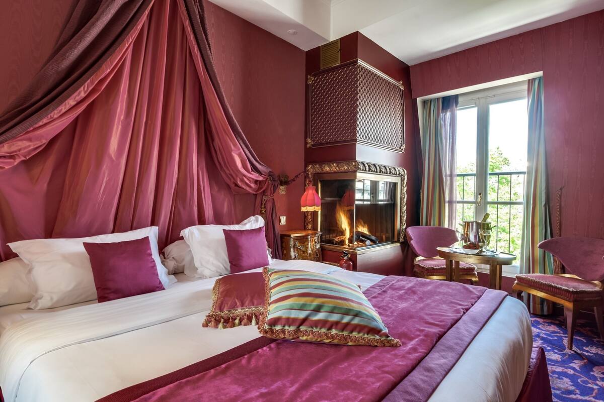 A luxurious bedroom with a large bed, a fireplace, a balcony view, and a cozy seating area.