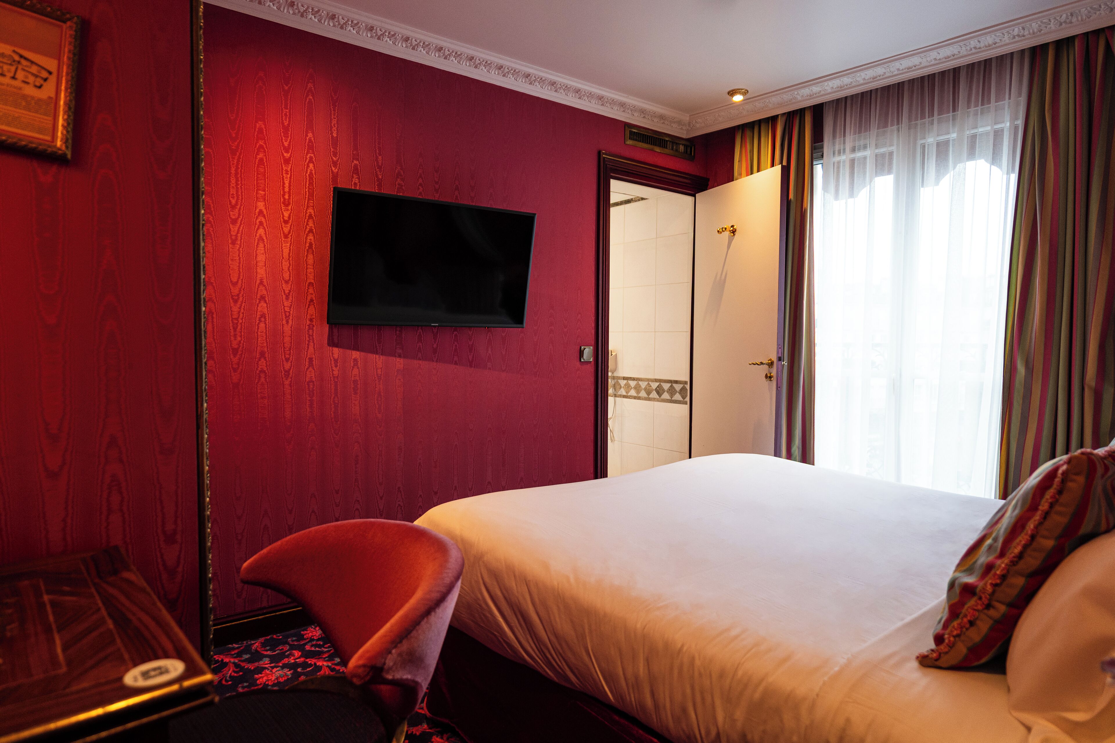 Une chambre d’hôtel avec un grand lit, un téléviseur fixé au mur, un bureau avec une chaise et une fenêtre avec des rideaux.