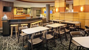 A hotel lobby with a reception desk, multiple tables and chairs, a flat-screen TV, and a decorative wall with a light fixture. - SpringHill Suites by Marriott Savannah I-95 (Savannah)